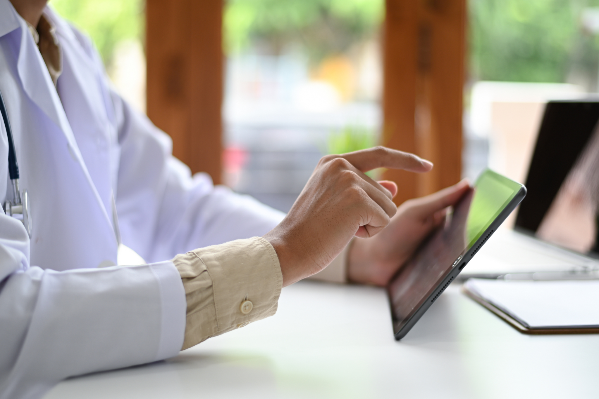 Close up of a clinician in a white coat tapping a tablet at a desk