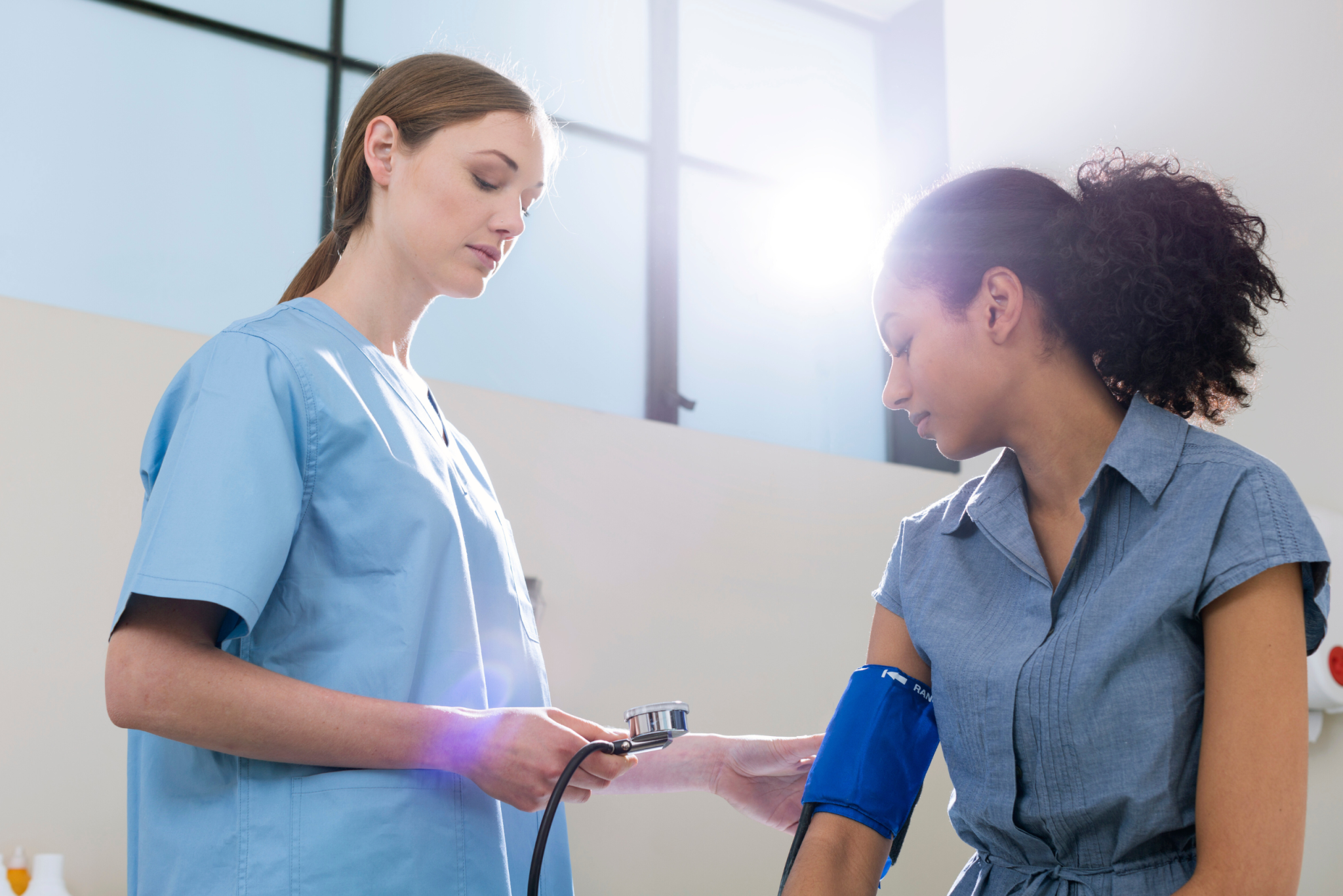 Nurse in blue scrubs taking a patient's blood pressure with a manual cuff