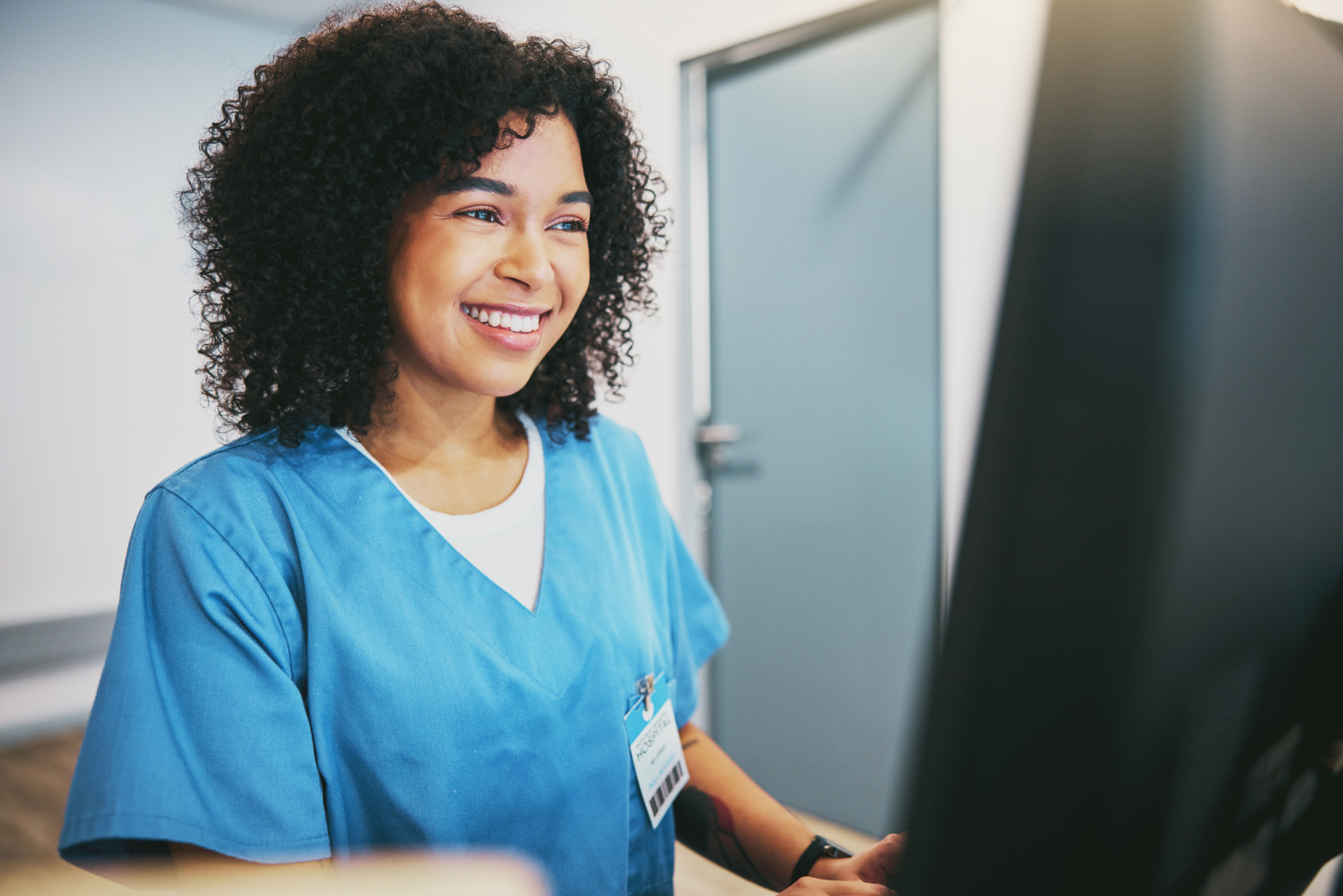 Smiling nurse in blue scrubs working at a computer